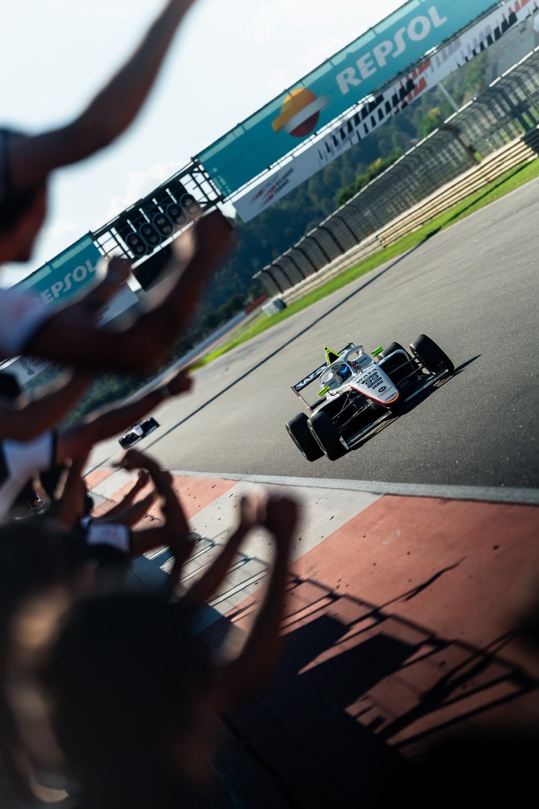Formula 4 car crossing the finish line while the team celebrates on the pit wall